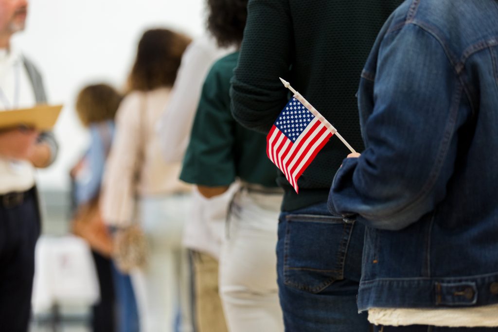 Diverse group in line to vote; one holds American flag