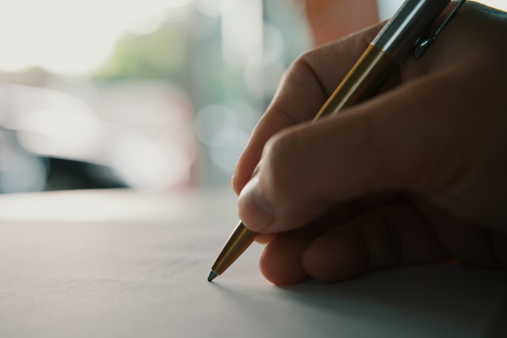 Businessman holding pen writing on paper for new appointments information in organizer concept, male hands making notes in personal paper planner at desk, close up view