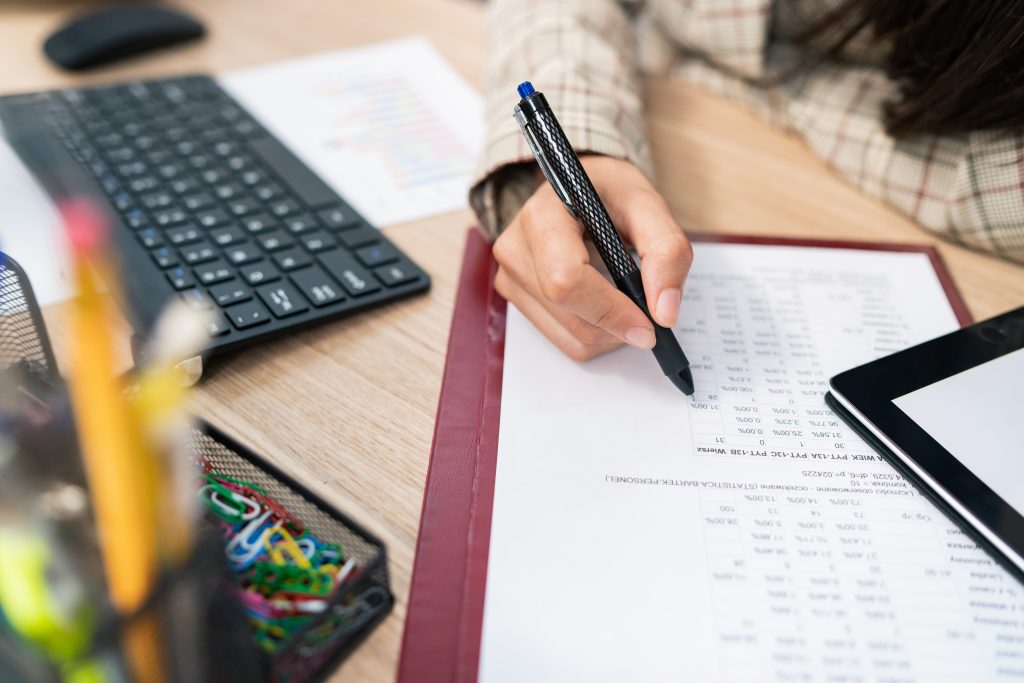 Close-up on a document, statistical table, company's calculations, an office accountant sits at the desk filling in the right places, checking the correctness, touches the paper with a pen