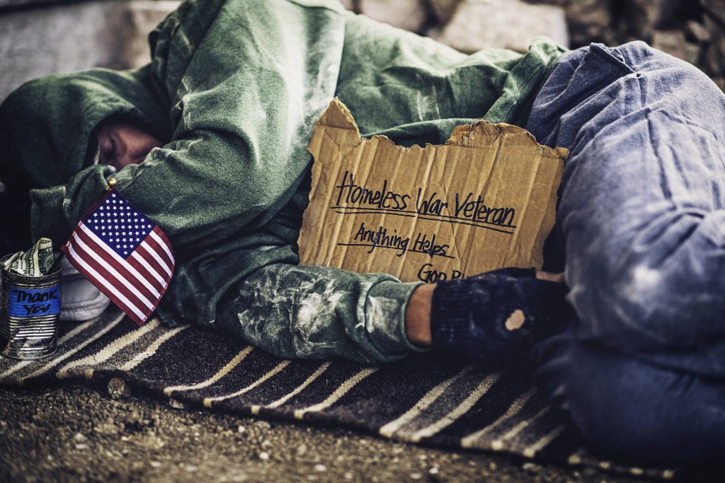 Fighting adversity. Homeless war veteran sleeping with sign and money tin (Getty Images CatLane)