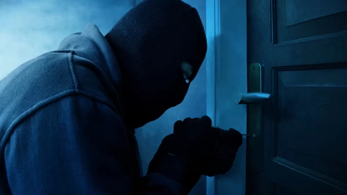 Masked thief using lock picker to open locked door