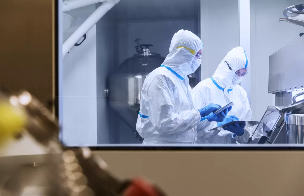 Scientists in clean suits using digital tablets in experiment in laboratory