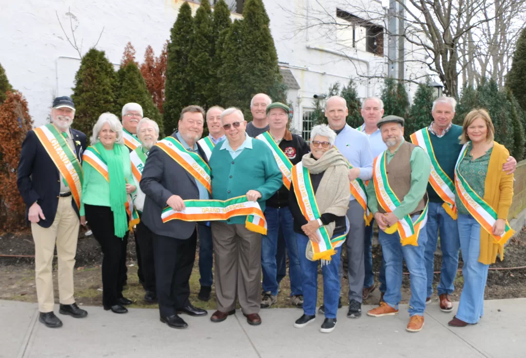 (Photo by Hank Russell) Dennis Smith (front, third from left), who served as Grand Marshal in
the 2022 St. Patrick’s Day Parade, passes the sash to Deacon Marty McIndoe (front, fourth from
left) at a special ceremony at The Tap Room on February 26.