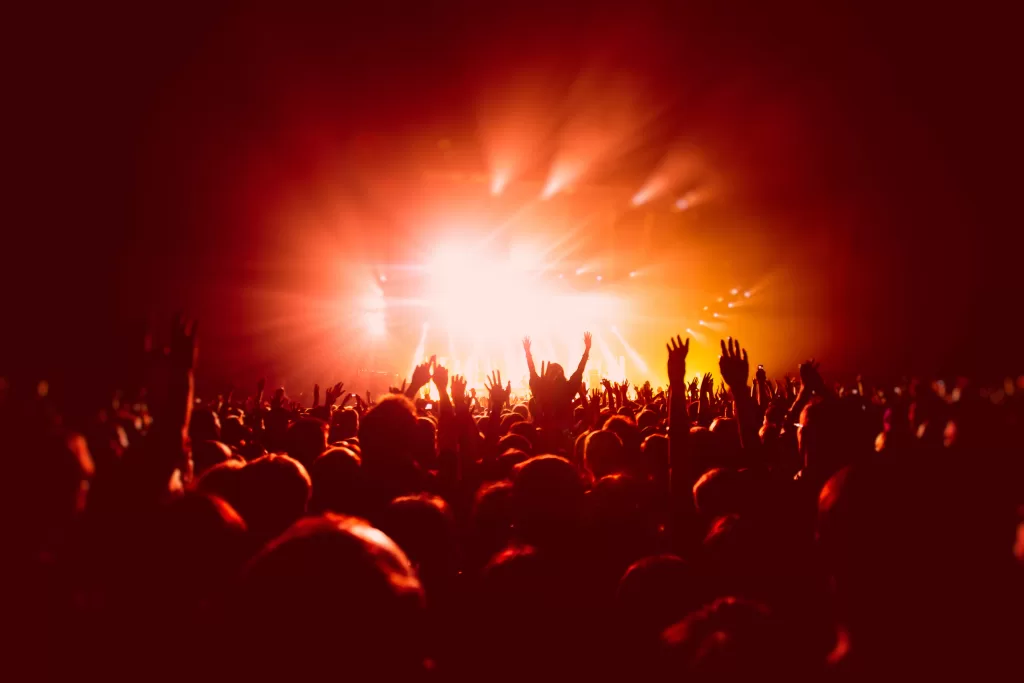 A crowded concert hall with scene stage in red lights, rock show performance, with people silhouette, colourful confetti explosion fired on dance floor air during a concert festival