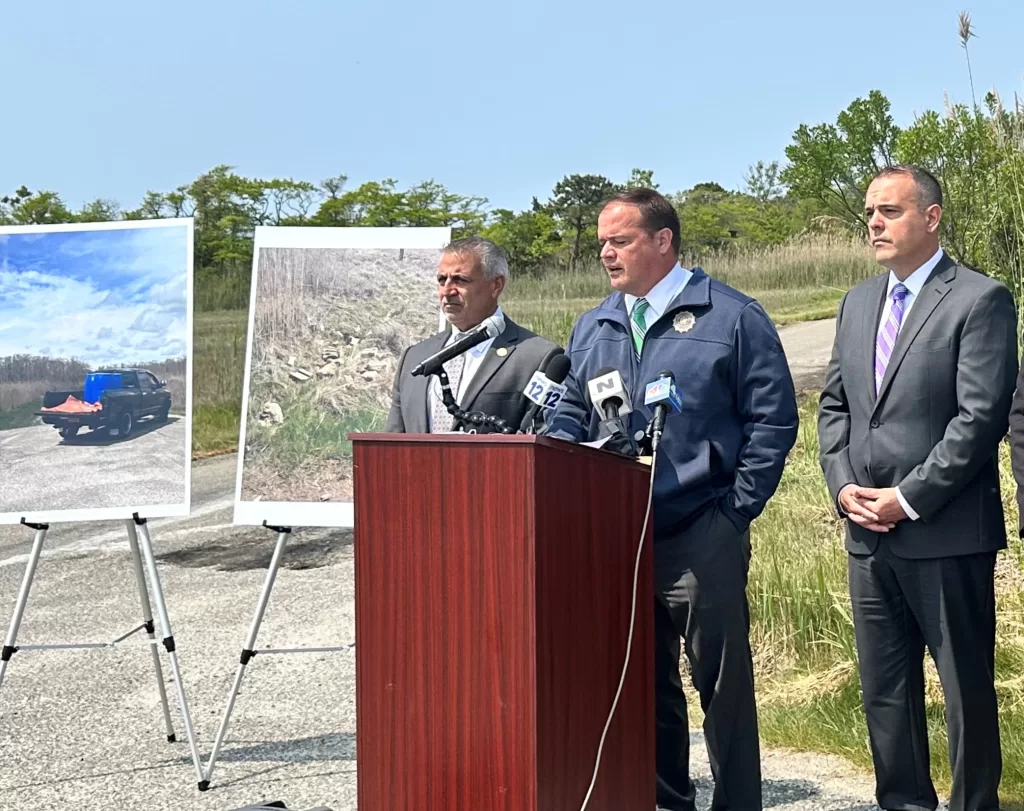 (Photo: Tania Lopez/Office of Suffolk County District Attorney Ray Tierney) Suffolk County District Attorney Ray Tierney (center) displays photographic evidence that led to the arrests of Fabio and Judith Monasterolo at a press conference on May 24 that took place in Mastic Beach, where the alleged illegal dumping took place. He is joined by Suffolk County Legislator Jim Mazzarella (left) and Brookhaven Town Deputy Supervisor Dan Panico (right).