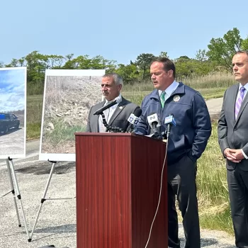 (Photo: Tania Lopez/Office of Suffolk County District Attorney Ray Tierney) Suffolk County District Attorney Ray Tierney (center) displays photographic evidence that led to the arrests of Fabio and Judith Monasterolo at a press conference on May 24 that took place in Mastic Beach, where the alleged illegal dumping took place. He is joined by Suffolk County Legislator Jim Mazzarella (left) and Brookhaven Town Deputy Supervisor Dan Panico (right).