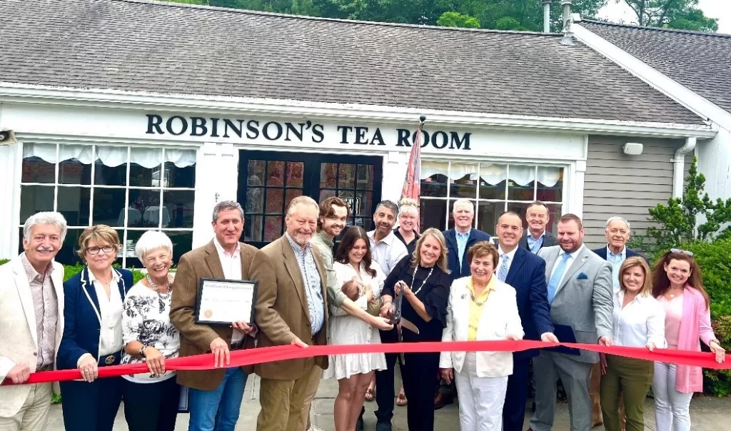 (Photo: Town of Brookhaven) Brookhaven Town Councilman Jonathan Kornreich (fourth from left), Deputy Supervisor Dan Panico (sixth from right) and New York State Assemblyman Ed Flood (fourth from right) take part in the ribbon cutting for Robinson’s Tea Room.