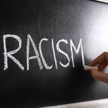 Hand writing the word racism on blackboard. Stop hate. Against prejudice and violence. Lecture about discrimination in school.