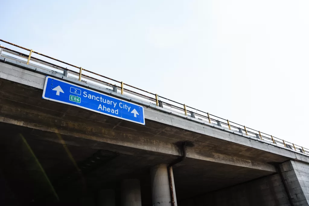 Sanctuary City Ahead Blue Road Sign Against Clear Sky