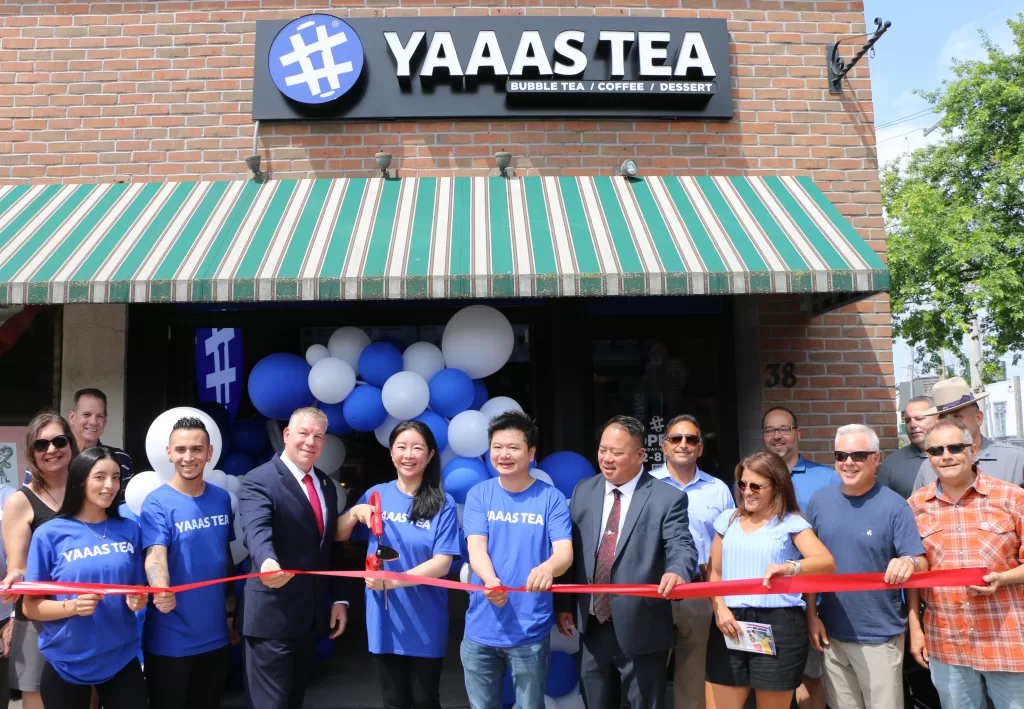 (Photo by Hank Russell) YAAAS TEA President/CEO Kelly Zhou (fourth from left) cuts the ribbon to celebrate the grand opening of her fourth shop in Patchogue. Also pictured (left to right): Employees Maira Velanzia and Juan David Sanchez; Suffolk County Deputy Commissioner Anthony Carter, YAAAS TEA Co-Founder Evan Chen, Suffolk County Police Asian Jade Society President Ed Hugh, Greater Patchogue Chamber of Commerce Board Members Karen Drago and Terry Tuthill and Greater Patchogue Chamber of Commerce Executive Director David Kennedy. 
Standing behind Ms. Velanzia: Greater Patchogue Chamber of Commerce President Dawn Turnbull. Standing behind Ms. DragoL Mike Napolitano, chief of state for New York State Senator Dean Murray, and Greater Patchogue Chamber of Commerce Board Member James Diele-Stein.