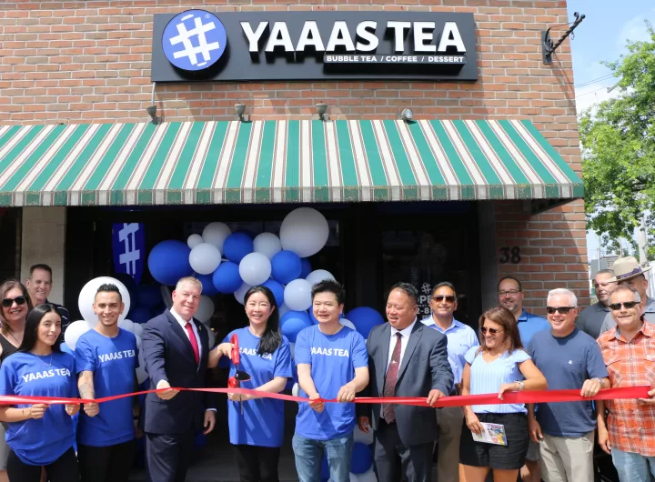 (Photo by Hank Russell) YAAAS TEA President/CEO Kelly Zhou (fourth from left) cuts the ribbon to celebrate the grand opening of her fourth shop in Patchogue. Also pictured (left to right): Employees Maira Velanzia and Juan David Sanchez; Suffolk County Deputy Commissioner Anthony Carter, YAAAS TEA Co-Founder Evan Chen, Suffolk County Police Asian Jade Society President Ed Hugh, Greater Patchogue Chamber of Commerce Board Members Karen Drago and Terry Tuthill and Greater Patchogue Chamber of Commerce Executive Director David Kennedy. 
Standing behind Ms. Velanzia: Greater Patchogue Chamber of Commerce President Dawn Turnbull. Standing behind Ms. DragoL Mike Napolitano, chief of state for New York State Senator Dean Murray, and Greater Patchogue Chamber of Commerce Board Member James Diele-Stein.