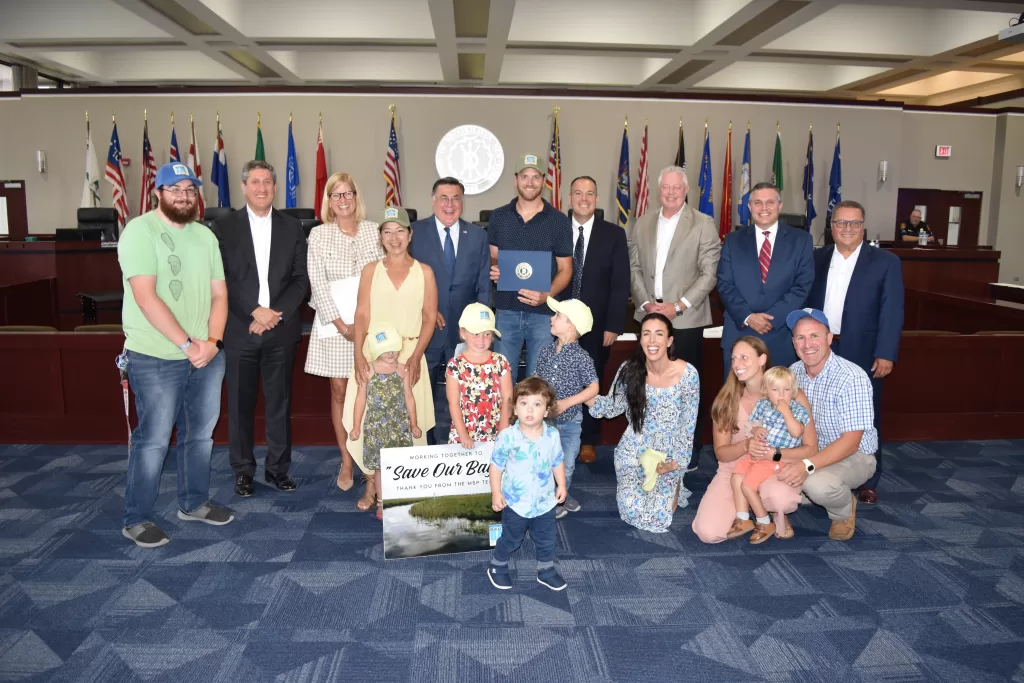 (Photo: Town of Brookhaven) Pictured in the back row, left to right are Anthony Sferrazza; Councilmember Jonathan Kornreich;
Councilwoman Jane Bonner; Laura Frabizio; Supervisor Ed Romaine; Town of Brookhaven Bay Management
Specialist I and Moriches Bay Project member, Dwight Surgan; Deputy Supervisor Dan Panico; Councilman
Neil Foley, Town Clerk Kevin LaValle and Councilman Michael Loguercio. Pictured in the front row, left to
right are Ruby Jeanes; Lily Jeanes; Nico Surgan; Mack Surgan; Cara Surgan; Christa Jeanes; Christian Jeanes
and Jonathan Jeanes.