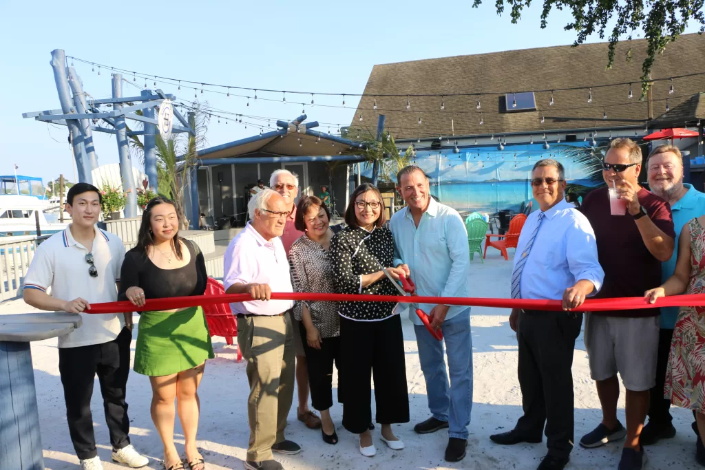 (Photo by Hank Russell) Baja Boathouse co-owners Hong Liu (center) and Lenny Oliva (fourth from right) cut  the ribbon on the grand opening of their cantina/restaurant/marina in Patchogue on August 9. Also pictured (left to right): Liu’s son Vinci and her daughter Emmy, Patchogue Village Mayor Paul Pontieri, Liu’s friend Eileen Lin, Suffolk County Legislator Dominick Thorne, customer Bruce Rosenberg and Patchogue Village Business Improvement District Executive Director Dennis Smith.