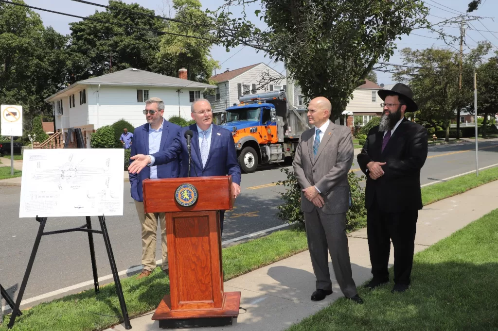 (Photo: Office of Legislator William Gaylor) Nassau County Legislator William Gaylor (standing behind podium) is joined by Legislator John Giuffré (second from right) and Rabbi Elon Soniker (right) of Congregation Anshei Shalom of West Hempstead.