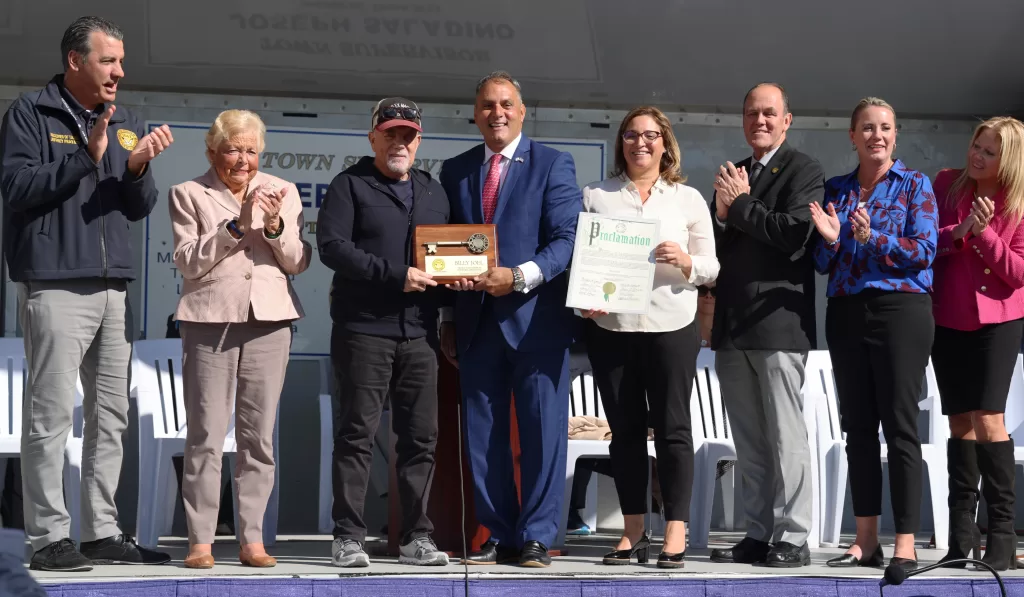 (Photo: Town of Oyster Bay) Oyster Bay Town Supervisor Joseph Saladino (fourth from left) presents Billy Joel (third from left) with a key to the town during the dedication of Billy Joel Way on October 19.