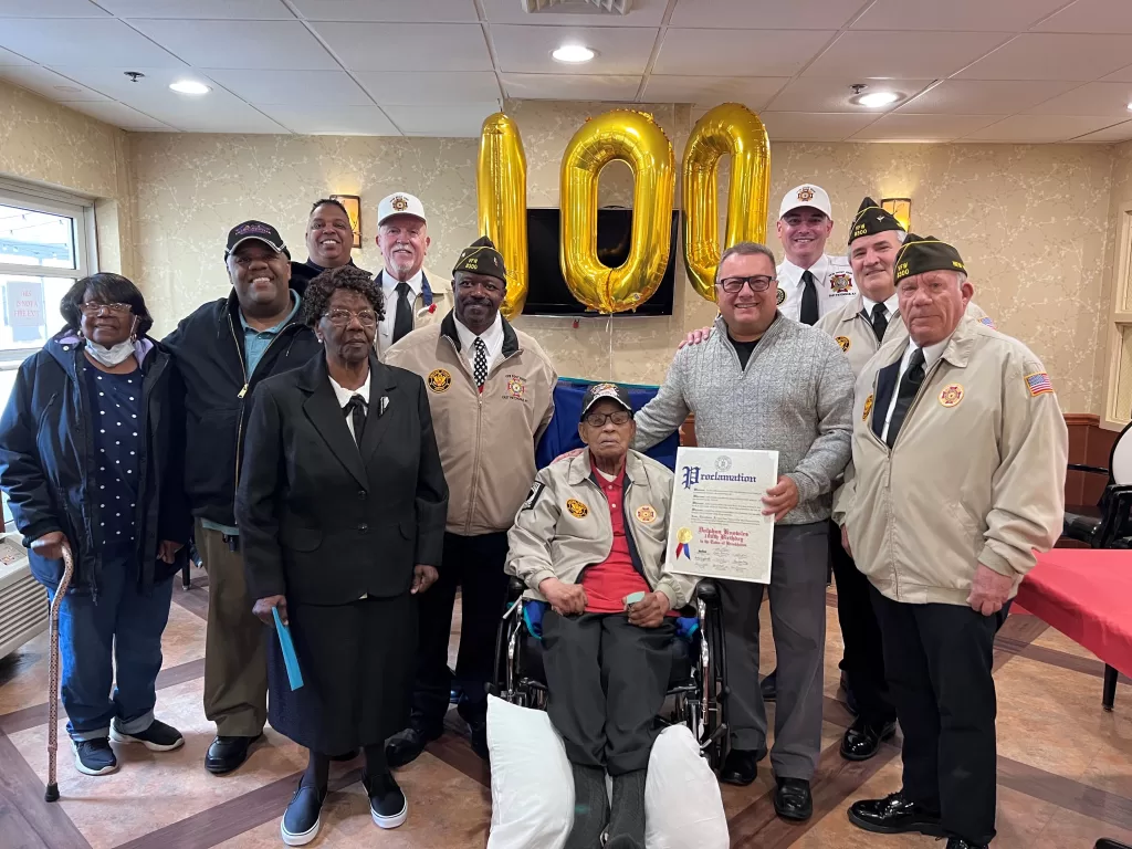 (Photo: Town of Brookhaven) Brookhaven Town Councilman Michael Loguercio (standing, second from right) presents a proclamation honoring World War II veteran Dolphus Knowles (sitting) on his 100th birthday. Knowles is joined by his wife (standing, second from left) and members of VFW Post 8300.