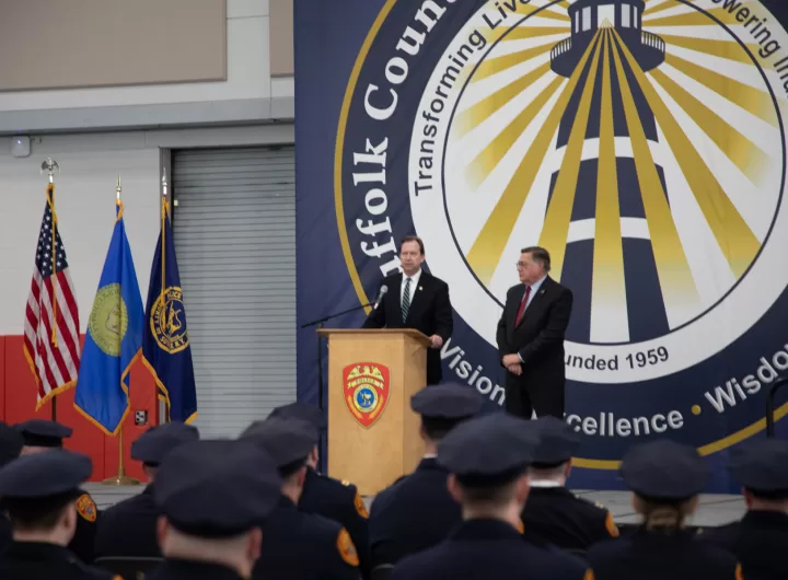 (Photo Courtesy of SCPD) Suffolk County Acting Police Commissioner Robert Waring (standing behind podium) addresses the police officers while County Executive Ed Romaine looks on.