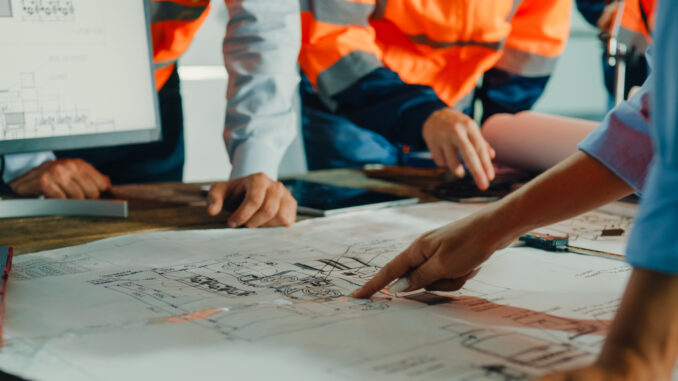 Closeup of team of industrial engineers meeting analyze machinery blueprints consult project on table in manufacturing factory. Working in manufacturing plant or production plant.