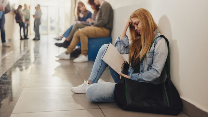 Female student relaxing on floor during a break in a hallway.