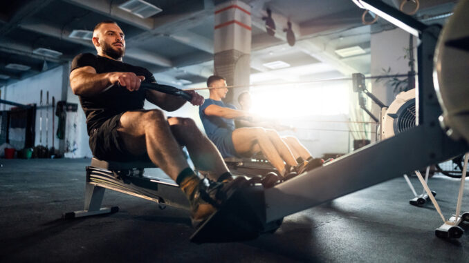 Male athletes exercise on a rowing machine at the gym