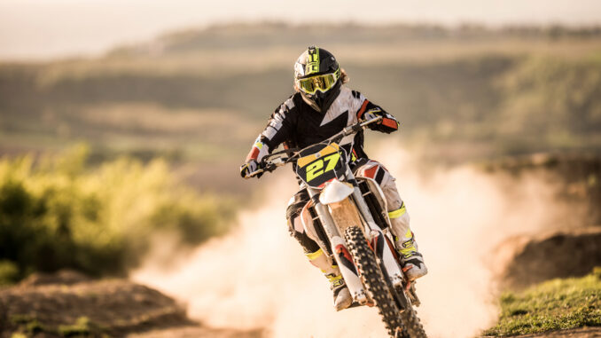 Man on dirt bike racing on dirt road in nature.