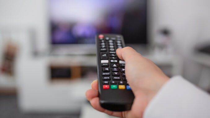 Watching TV and using remote controller. Hand with remote controller changing channels or opening apps on smart tv